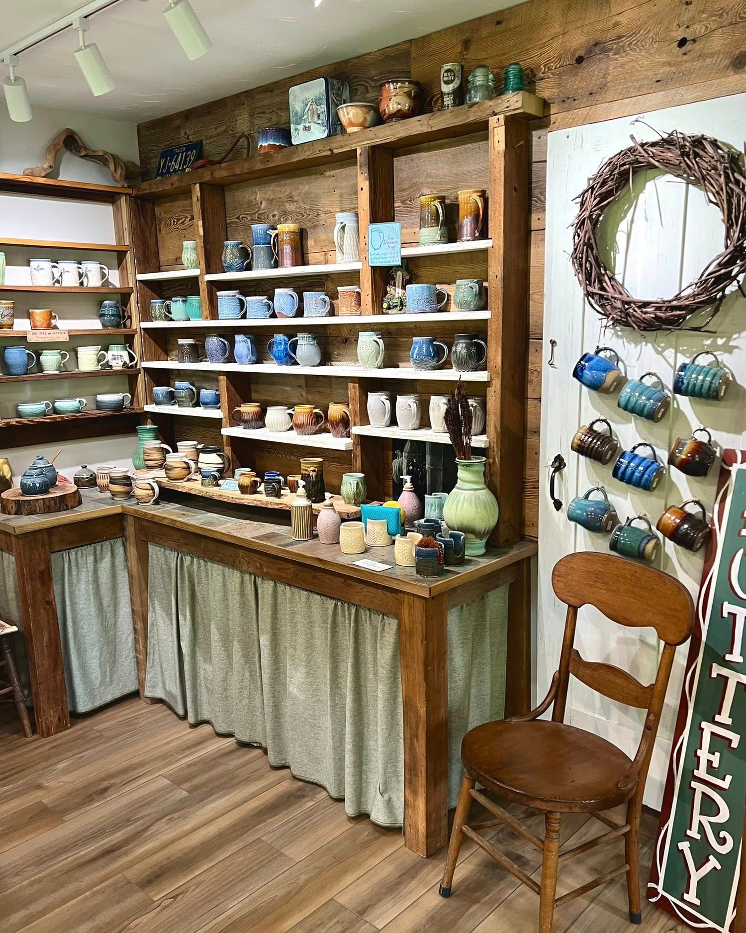 Ceramic mug display in a store with shelves and a chair.