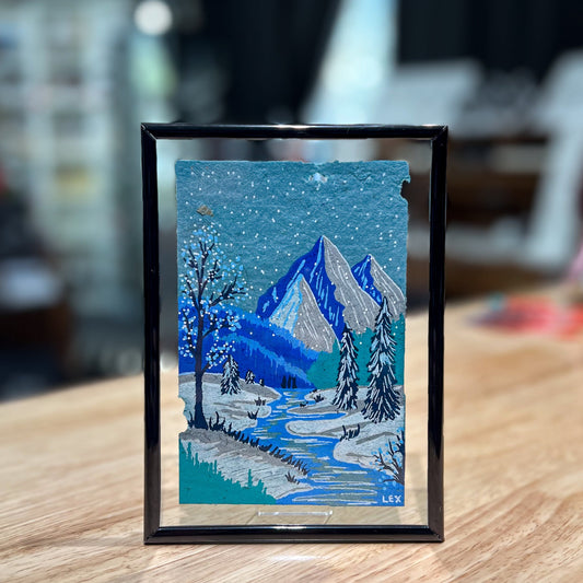 Framed artwork of a snowy mountain landscape on a wooden surface.